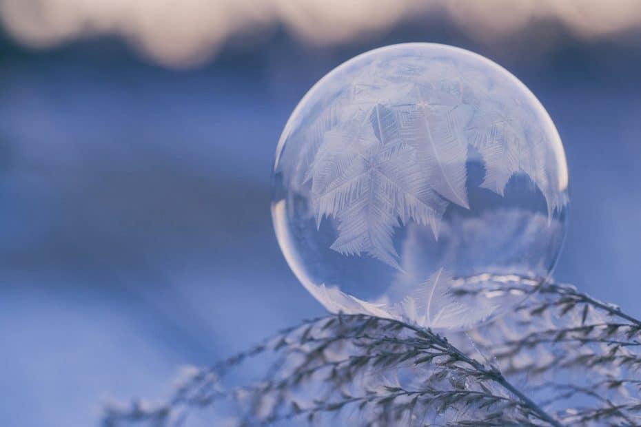 A frozen soap bubble with intricate ice crystals sits on dried grass, echoing the peaceful chill just outside a tent on a winter camping trip.